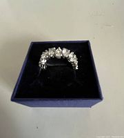 Front view of the Swarovski ring with clear, white, droplet-shaped stones set in a silver-tone band inside a presentation box.