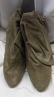 Close-up photo showing a pair of green suede boots with slouchy design, displaying texture and pointed toe shape.