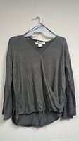 Front view of a dark grey women's long sleeve V-neck shirt hanging on a hanger