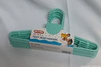 Photo of green plastic baby hangers with packaging labeled 'Set of 8 Teddy Bear Hangers' by Baby's N Twins.