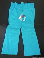 Front view of a single blue snow pant showing elastic waistband and snap closure