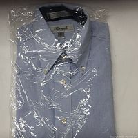 Photo showing light blue Forsyth brand dress shirt folded and sealed in clear plastic factory packaging.