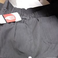 Close-up of black pinstripe chef pants showing elastic waistband, front pocket, and factory tag.