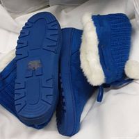 Close-up of one pair of royal blue women's knitted boots showing knit upper, faux fur lining, and side lace with pom-poms