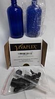 Two 16 oz cobalt blue glass bottles, one unwrapped and one with bubble wrap, displayed on top of a Vivaplex branded box. A resealable plastic bag containing multiple black plastic spray triggers with attached dip tubes is in front of the box.