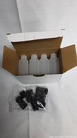 Box of clear 2 oz plastic squeeze bottles, open to show bottles inside and a separate bag of black flip top caps.