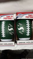 Two green football-shaped drink holders in original packaging with Saskatchewan Roughriders logo, labeled as 'Drink Holder' and 'Game On Football'.