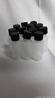 Ten 2 oz clear plastic squeeze bottles with black caps arranged in group, showing bottle shape and cap detail.