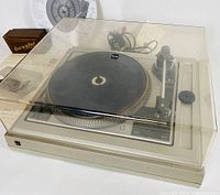 Clear plastic dust cover with small crack on the back over a Dual CS 1258 turntable with black platter and visible tonearm.