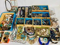 Overhead view of multiple small boxes and trays filled with assorted necklaces, bracelets, earrings, rings and brooches