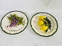 Front view of two 12-inch Eva Gordon pottery wall plates with 3D food art, one with grapes and one with lemons
