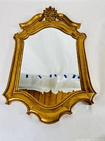 Front view of ornate gold wall mirror with shell motif on top.