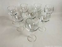 Eight clear vintage glass stemware wine glasses arranged in two rows showing their rounded shape and elongated stems.