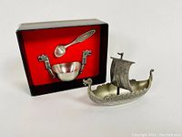Photo of the three items in the lot showing the Viking ship shaped salt dish, the open salt bowl with two dragon head handles, and the matching spoon inside the original box with red velvet lining.