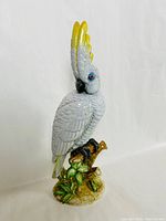 Side angled view of the white cockatoo figurine mounted on a branch base showing detailed feathers and yellow crest.
