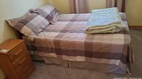 Fully made double size bed showing plaid duvet cover, matching pillowcases, bed skirt, and part of the frame visible.