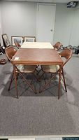 Photo showing all four brown folding chairs arranged around two square folding card tables with different laminate tops, one dark brown wood-patterned and one lighter beige.