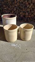 Front view of all three stoneware pots on concrete with stacked firewood background. Two smaller numbered 3 pots and one larger numbered 6 pot.