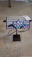 Full view of the Tiffany-style stained glass desk lamp on a concrete floor.