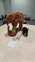 Photo showing the full lot of three figures including a large wooden elephant with an 8-inch height sticker and two smaller stone elephants in black and white.