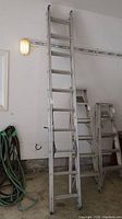 Full view of two-section aluminum extension ladder standing upright against wall