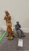 Three decorative figures displayed together, including a blue papier mache figure seated on rock, a carved wood standing figure, and an orange figure