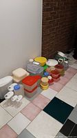 Wide view of plastic containers, jugs, colanders, lettuce spinner, steamer, and glass measuring cups grouped on tiled floor