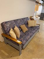Front and side views of the wooden futon showing the mattress and cushions with details of the wooden armrests and the pattern on the mattress.