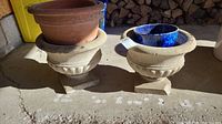 Two large beige cement-form planters with one clay pot placed on top of one of them.