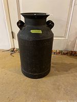 Front view of the vintage black painted milk can showing its overall shape and condition.