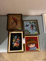 Four framed needlepoint artworks showing birds, flowers, and a child portrait.