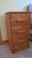 Full view of the night stand showing three drawers with rectangular handles and light wood finish.