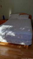 Queen size Shermag wooden bed frame with mattress, box spring, and white bedding including pillows and shams on hardwood floor.