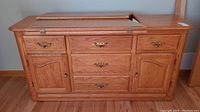 Front view of the wooden dresser showing drawers, cabinets, and partially open hinged top.