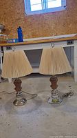 Pair of wood and metal base table lamps with pleated fabric shades, shown side by side on floor.