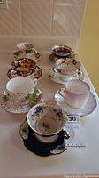 Eight different vintage tea cups and saucers with ornate floral and gold detailing.