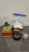 Lot overview showing glass chocolate fondue pot, wooden box, green-yellow art glass dish, trinket box, tea light candles in plastic box, and bag of additional candles.