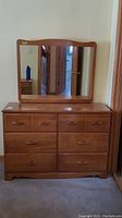 Full front view of the wooden dresser with attached mirror showing six drawers and reflection in the mirror.