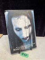 Front cover photo of the vintage 1998 Marilyn Manson book showing a close-up photo of the artist's face with stylized makeup and geometric overlay.