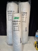 Three white pillows in plastic packaging, one smaller square 50x50 cm (20x20 inches) and two larger 65x65 cm (26x26 inches). Labeled IKEA FJÄDRAR.