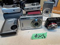 Front and top views of various compact digital cameras showing brands Sony, Canon, and Acer with some cases and lens details.