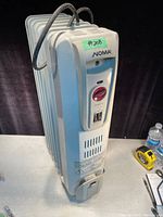 Front angled view of the white NOMA oil-filled radiator heater showing thermostat dial, controls, and ventilation slots.