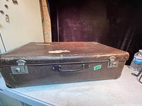 Exterior view of the vintage brown suitcase showing metal latches, handle, and surface wear.