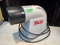 Side view of the Art Tracer Projector showing white plastic body with black lens and attached power cord.