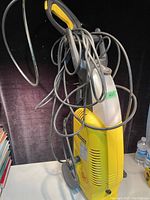 Photo of the KARCHER power washer showing its yellow body with gray handle and coiled cords hanging from it