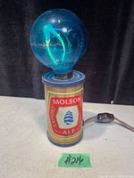 Photo of a Mid-Century Modern Molson Export Ale beer can table lamp with a blue decorative bulb. Lamp is approx 8.5 inches tall and includes inline switch on power cord.