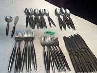 Photo showing the partial Mid Century Modern stainless steel cutlery set arranged on a surface with multiple teaspoons, soup spoons, knives, dessert forks, and dinner forks visible.