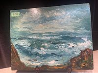 Front view of vintage oil on board painting showing a stormy sea with rocky foreground.