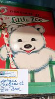 Close-up photo of the book's box front showing a white bear cub holding a candy cane with title 'Christmas at the Little Zoo'.