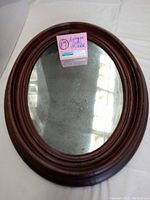Full view of the antique oval mirror with wood frame showing overall condition and reflections.